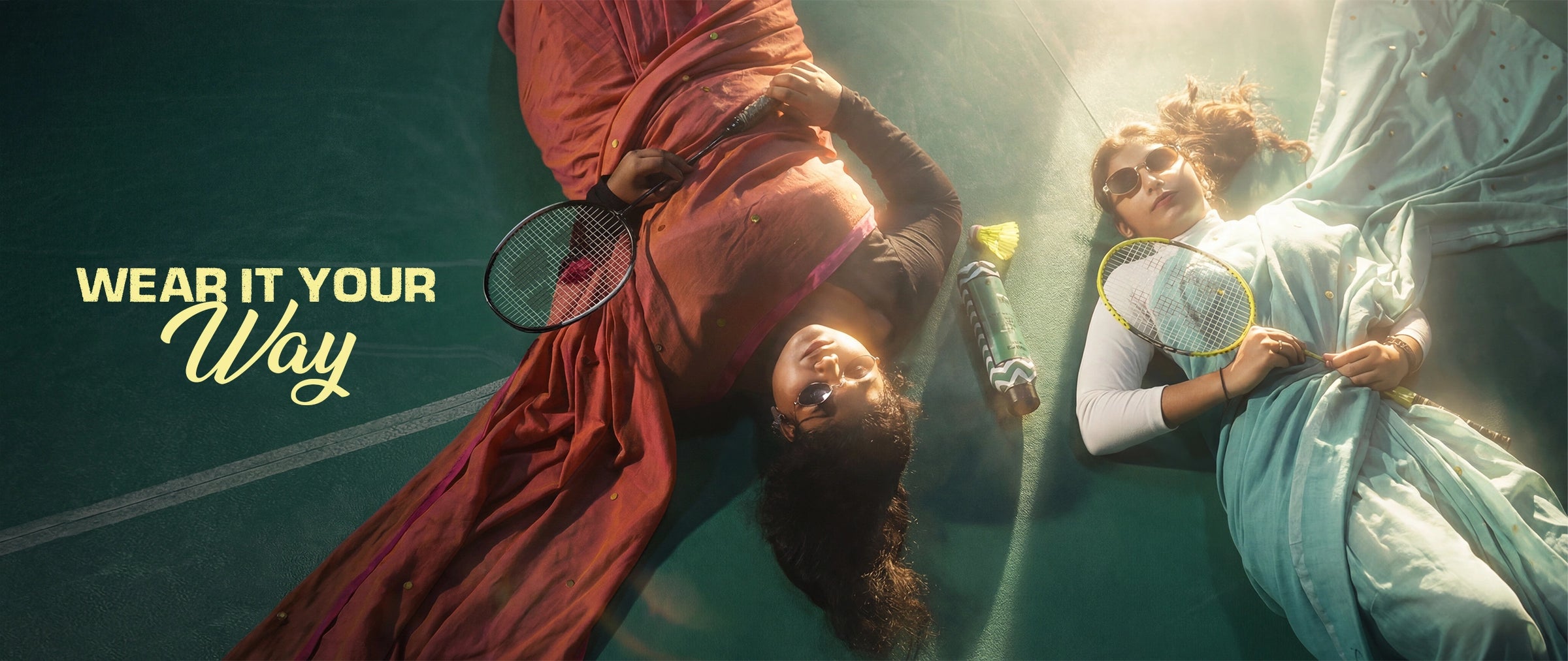Two women lying on a badminton court wearing statement sarees with sunglasses and sports gear, Kottanz Loom Co